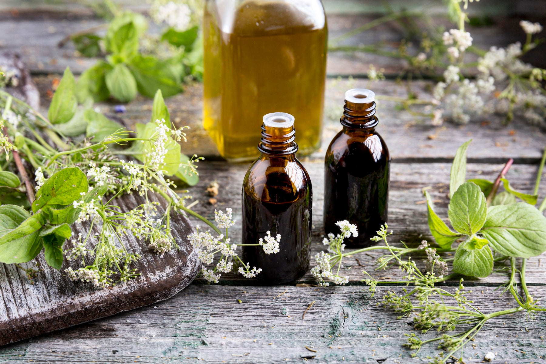 Bouteilles en verre brun avec des fleurs et des herbes sur une table en bois rustique.